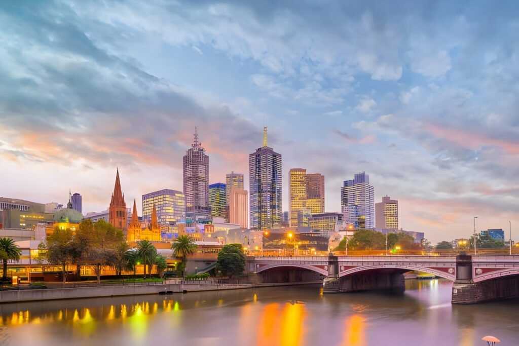City skyline of Melbourne at sunset, featuring a mix of modern skyscrapers and historic architecture along the Yarra River.